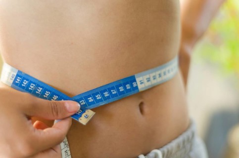 Skinny young woman measuring her slim waist with a measuring tape