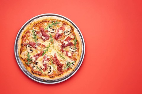 Pizza top view, homemade with prosciutto, arugula, champignons and mozzarella. Delicious ham pizza.