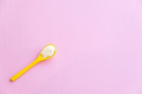 Spoon with sugar close-up on a pink background