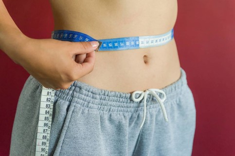 Skinny young woman measuring her slim waist with a measuring tape