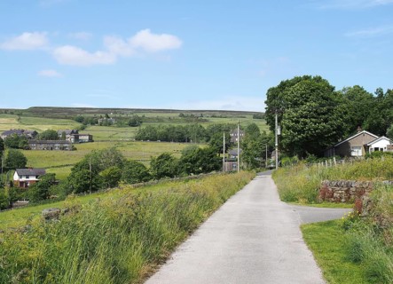 Narrow country lane with the village of wadworth and hillside fields near hebden bridge in
