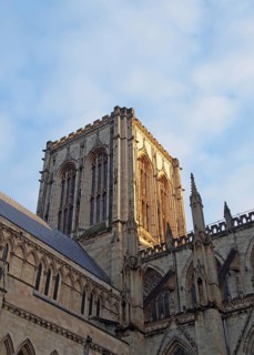 Side view of the central tower of york minster in sunlight against a blue cloudy sky