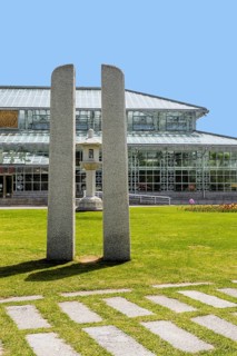 Modern architectural glass building with central stone sculpture, amid a green park setting and