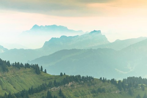 An impressive panorama of mountains with rocky peaks and dense forests under a cloudy sunset,