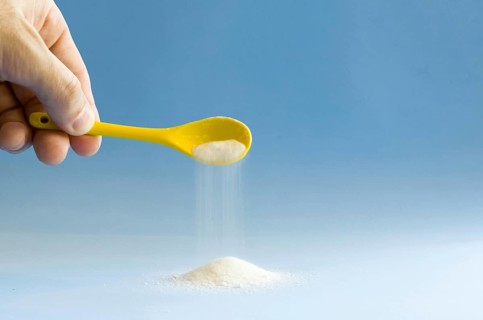 Yellow spoon turning sugar on blue background