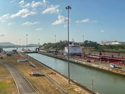 A ship moves through a canal surrounded by streets and lampposts. The atmosphere is calm and the