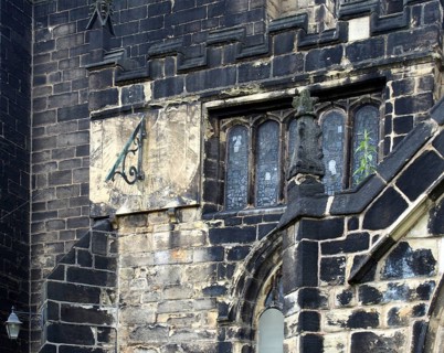 A full frame close up of ancient stonework stained glass windows and a sundial on the medieval