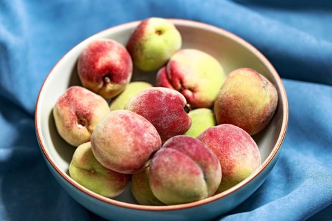 Vineyard peaches in a grey bowl on a blue background