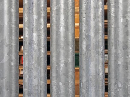 A close up of vertical galvanized steel fence with wooden pallets in outdoor storage visible