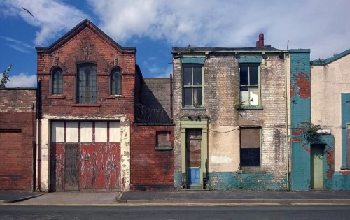 Derelict houses and abandoned commercial property on a residential street with boarded up windows
