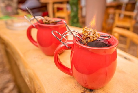 Image with a mug of hot wine, which has tongs with a flaming cone of sugar on top. It is a
