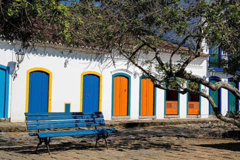 View to colonial house facades with colorful wooden doors in sunshine with a blue bench and tree
