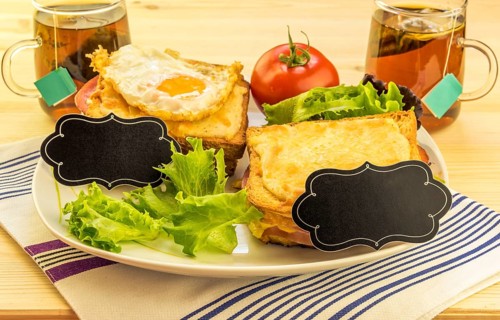 Plate with sandwiches, fried egg, tomato and green salad on wooden table. Each sandwich has a blank