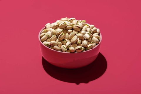 Pink bowl with roasted and salted pistachio minimalist on a magenta table. Bowl with pistachio