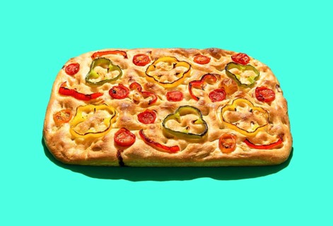 Homemade focaccia with vegetables and sourdough, in bright light minimalist on a green table.