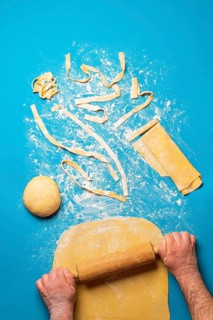 Man rolling semolina dough to make pasta, on a blue background. Top view of making tagliatelle