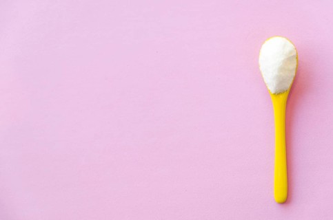 Spoon with sugar close-up on a pink background