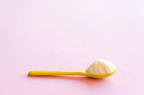 Spoon with sugar close-up on a pink background