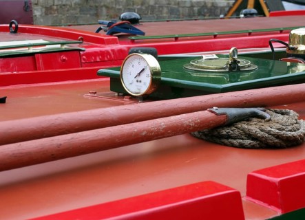 A close up of a brass gauge porthole boathooks and ropes on an old red canal narrow boat