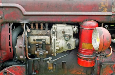 A close up of the engine of an old vintage tractor with red rusty bodywork and headlamp