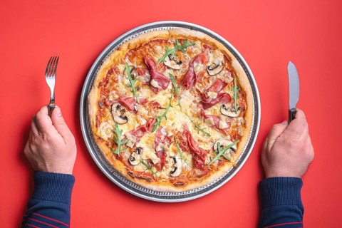 Man ready to eat a delicious homemade ham pizza. Top view with a prosciutto pizza on a red