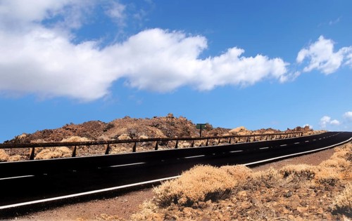Empty two lane black road stretching to the horizon in desert scrub with blue sky and white lane