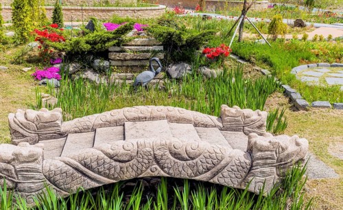 A stone bridge adorned with sculptures amidst plants and flowers in a colorful garden in Gyeongju,