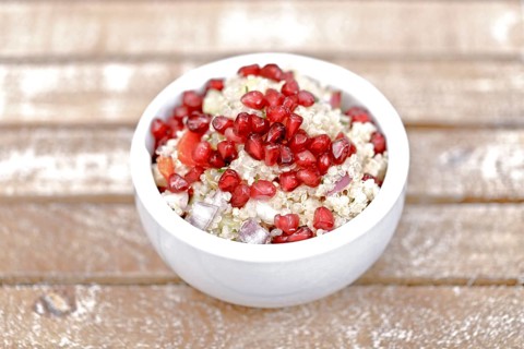Quinoa salad with pomegranate seeds, radiccio, cucumber and olives on a light brown background