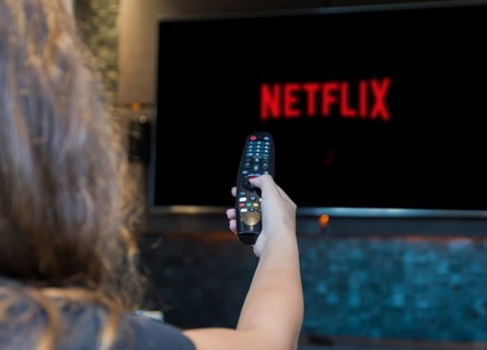 Young woman switching TV channels with remote control, Sars-CoV2 protective mask left in the corner