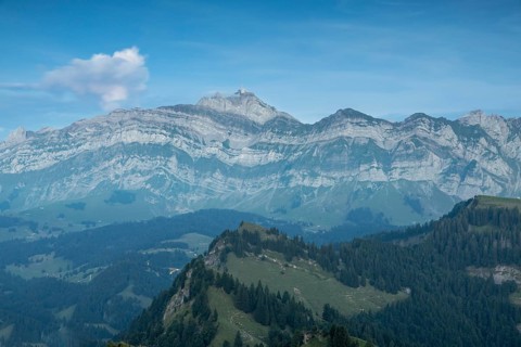 An impressive panorama of mountains with rocky peaks and dense forests under a cloudy sunset,