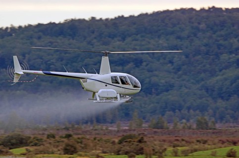 Helicopter spraying fertiliser on a crop in Westland, New Zealand, Oceania