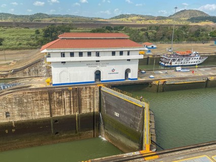 A picture of a lock with a large white building and a small boat. The surroundings are green and