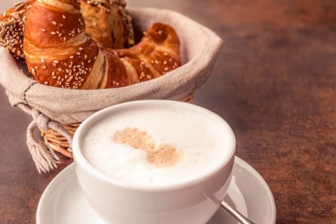 Delicious breakfast with a cup of milk coffee and fresh, sesame croissants in a rustic wicker