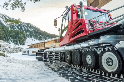 Tracked snow groomer car, parked near an alpine mansion, high in the Austrian Alps, near the