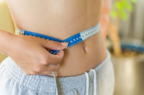 Skinny young woman measuring her slim waist with a measuring tape