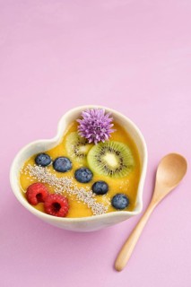 Peach smoothie bowl with blueberries, kiwi, white chia seeds and raspberries in a heart shaped bowl