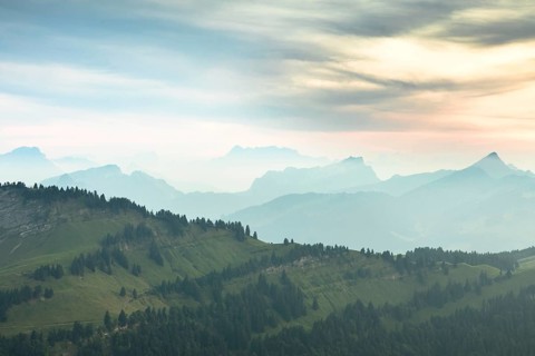 An impressive panorama of mountains with rocky peaks and dense forests under a cloudy sunset,