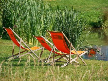 Three orange deckchairs on the banks of a pond in summer, papenburg, emsland, germany