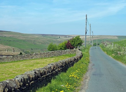 A narrow country lane surrounded by dy stone walls in a sunlit rural hilly landscape on the old