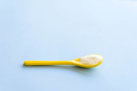 Spoon with sugar close-up on a light blue background