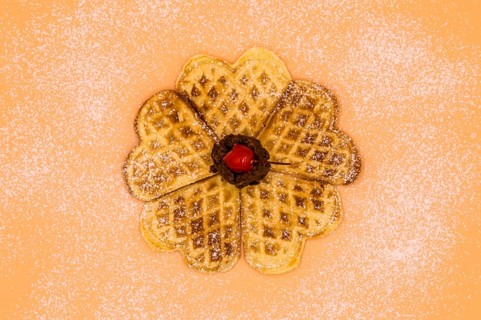 Homemade waffles with powdered sugar, a scoop of vanilla ice cream and a cherry on a pink