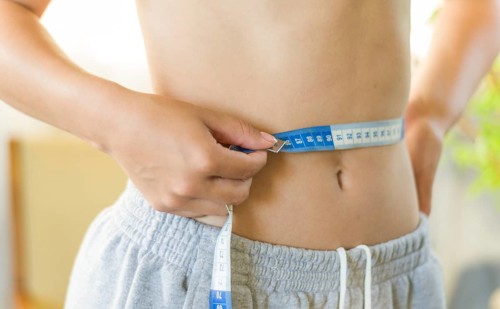 Skinny young woman measuring her slim waist with a measuring tape