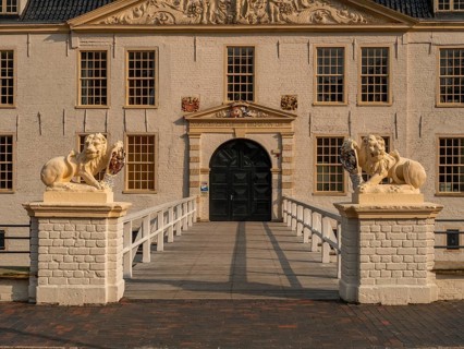 Elegant historic manor house with lion statues and decorative gable, accessible via a bridge,