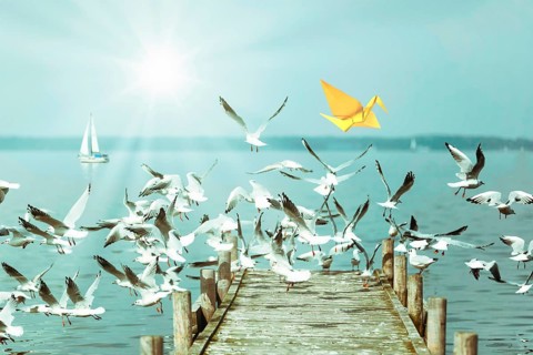Yellow origami bird and soaring seagulls, jetty on a lake