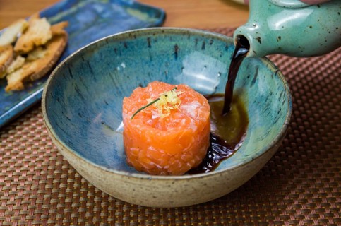 Man turning soy sauce into salmon tartare deliciousness in a beautiful decorated plate