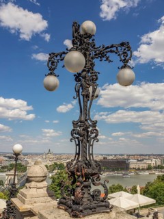 Artistically forged street lamp with ball lamps in front of a blue sky and a river in the