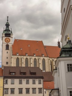 Gothic church with a striking clock tower and surrounding buildings under an overcast sky,