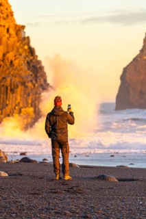 A tourist man taking a photo on the black sand beach of Reynisfjara at sunset in Iceland