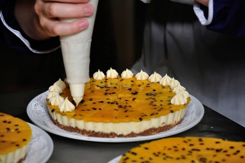 A cook adds whipped cream to a passionfruit cheesecake which will later be decorated with