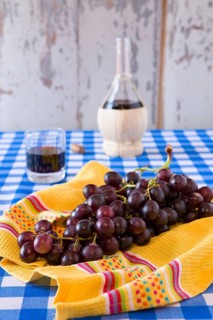 Bunch of red grapes and a glass of red wine with a wine flask on background over a checkered